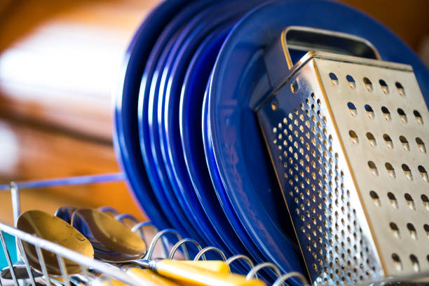 Close up color image depicting a collection of clean dishes and cutlery draining on the drying board in a domestic kitchen at home. Selective focus image with room for copy space.