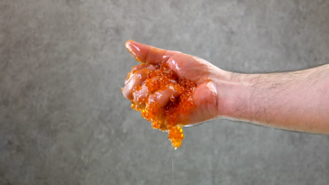 Male hand squeezes red caviar. Reveals palm. Close-up