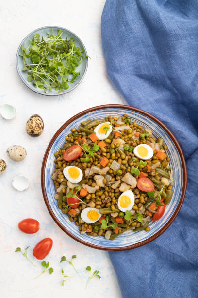 istock Mung bean porridge with quail eggs, tomatoes and microgreen sprouts on a white concrete background and blue textile. Top view, flat lay, close up. 1218939148