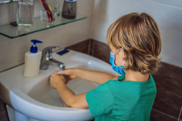 boy washes his hands with soap. boy in a medical mask due to coronavirus. pandemic. stay home. wash your hands - water human hand stream clean imagens e fotografias de stock