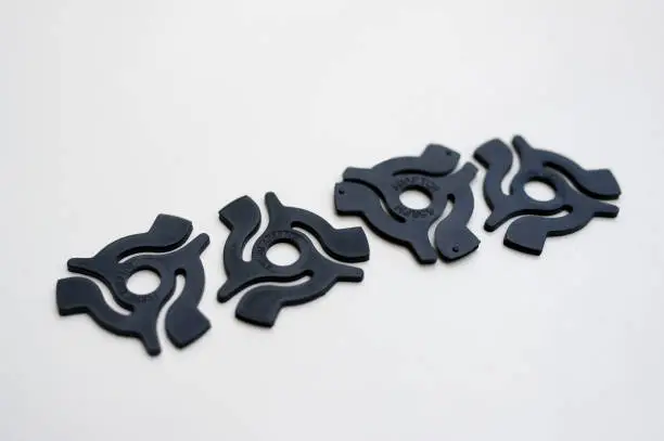 A row of four black plastic 45rpm record adaptors against a plain white background