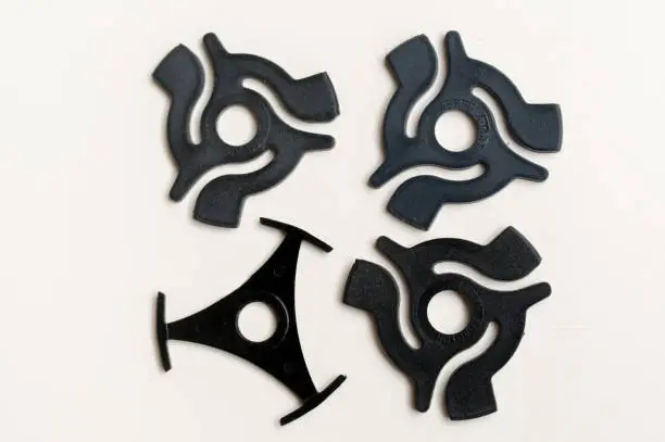 Three identical plastic 45rpm record adaptors and one different shaped adaptor shot from above against a plain white background