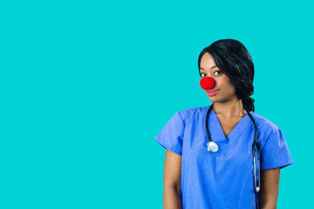 Portrait of a smiling female doctor or nurse wearing blue scrubs uniform and red nose looking at camera isolated on blue background Portrait of a smiling female doctor or nurse wearing blue scrubs uniform and red nose looking at camera isolated on blue background clown's nose stock pictures, royalty-free photos & images