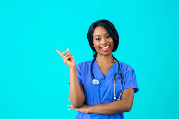 Portrait of a smiling female doctor or nurse in blue scrubs uniform looking at camera pointing at empty copy space Portrait of a smiling female doctor or nurse in blue scrubs uniform looking at camera pointing at empty copy space beckoning photos stock pictures, royalty-free photos & images