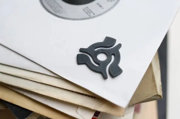 Close up of a 45rpm single record adaptor placed on the corner of a white single sleeve on top of a pile of old single sleeves