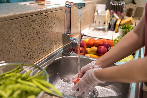 COVID-19, Coronavirus, Precaution, Part of a Series - Woman wearing gloves cleaning the fresh fruits in the kitchen sink