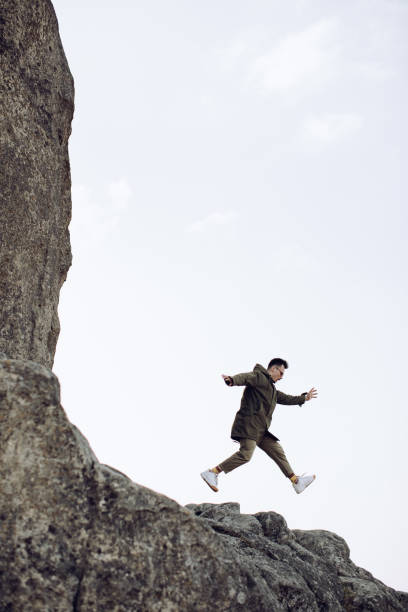 jeune homme heureux sautant hors de la roche. le concept de succès - on top of business cliff businessman photos et images de collection