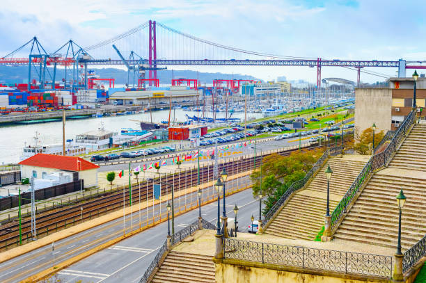 Paved stairs to commercial port of Lisbon at Tagus river, ships, cranes, containers, 25th April Bridge in background,