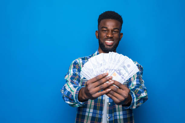 istock Cheerful young african man holding money banknotes over blue background 1218948376