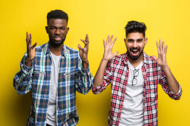 istock Two excited mixed race men friends screaming and raising hands while standing isolated over yellow background 1218950603