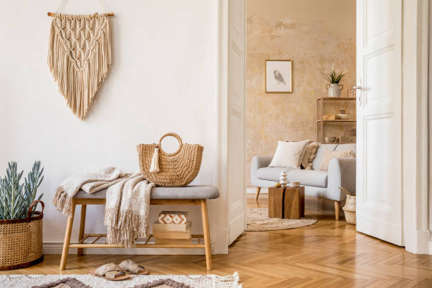 istock Scandinavian interior of open space with wooden bench, grey sofa, pillows, palid, picture frame, macrame, plant, books, carpet, decoration and elegant personal accessoreis in stylish home decor. 1218951849