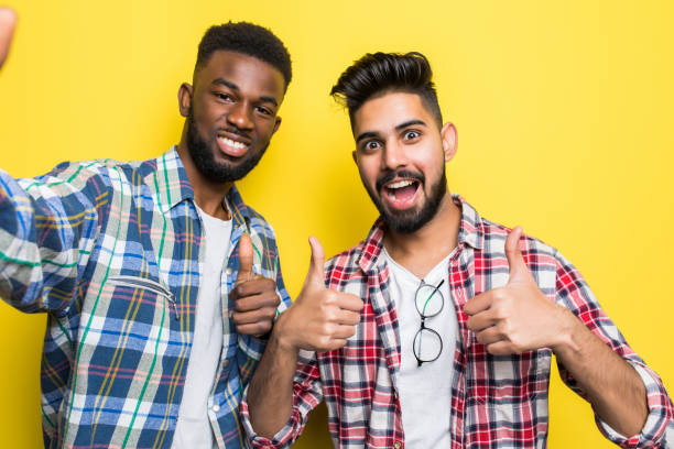 istock Portrait of a two mixed race men taking a selfie while standing together isolated over yellow background 1218952021