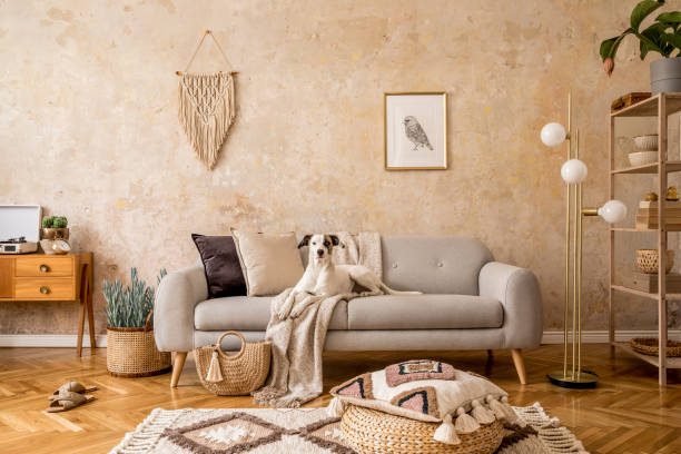 istock Stylish scandi compostion at living room interior with design sofa, commode, shelf, carpet, rattan pouf, plants, picture frame, macrame, personal accessories and dog lying on the couch. 1218952679