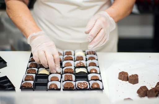 Close-up of female chocolatier arranging different chocolate candies in a plastic tray at confectionery store