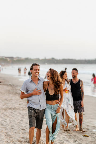 Discovering Kuta Beach Two couples walking down Kuta beach in Bali, Indonesia while embracing and laughing with each other. The main focus is the couple at the front. kuta beach stock pictures, royalty-free photos & images