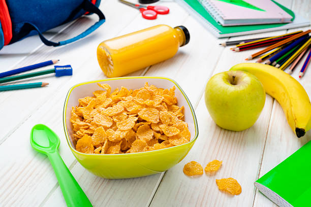 Healthy food for kids concepts: breakfast cereal in a green bowl shot on white table. An apple, banana and fruit juice ere beside the bowl. School supplies are at background. High resolution 42Mp studio digital capture taken with SONY A7rII and Zeiss Batis 40mm F2.0 CF lens