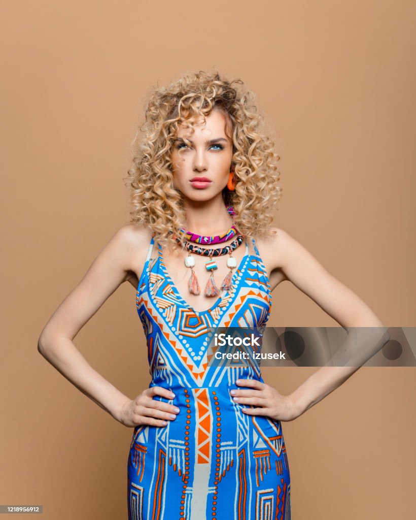 Fashion portrait of woman in boho style outfit Summer portrait of beautiful long curly hair young woman wearing boho style dress and jewelry. Studio shot on brown background. Adult Stock Photo