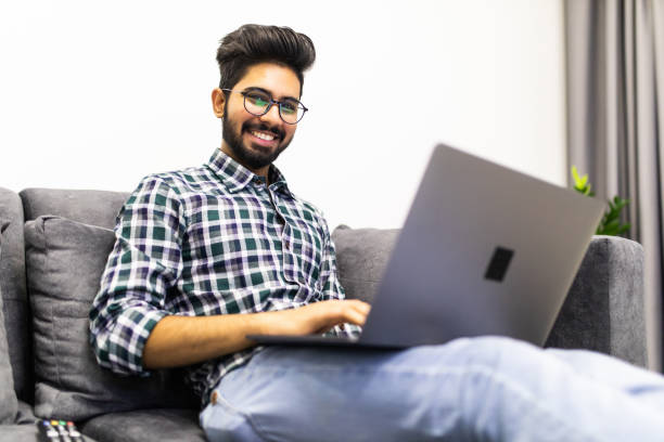istock Indian bearded man relaxing on sofa with laptop at home 1218959313