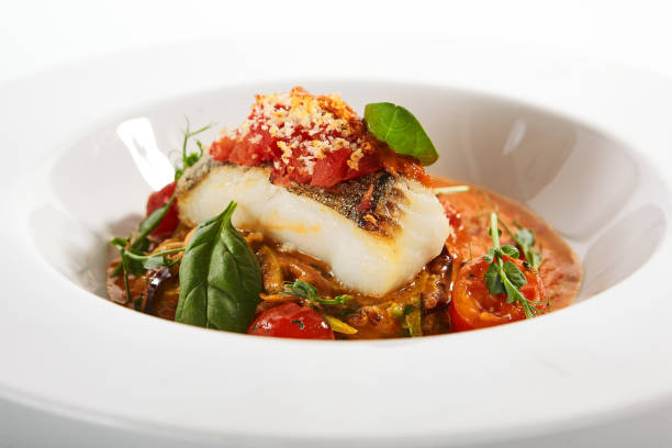 Halibut steak in crispy breading close up. Served cuisine. Dish with fish fillet and zucchini spaghetti in tomato sauce in white plate isolated. Restaurant food portion, delicious supper, main course