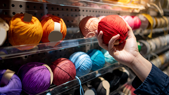 Male hand choosing red yarn ball in knitting shop or needlework shop. Selection of colorful yarn wool on shopfront. Shopping lifestyle concept