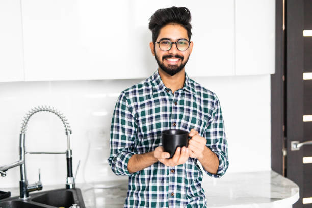 istock Handsome indian bearded man on kitchen is smiling and drinking coffee in the morning. 1218960164