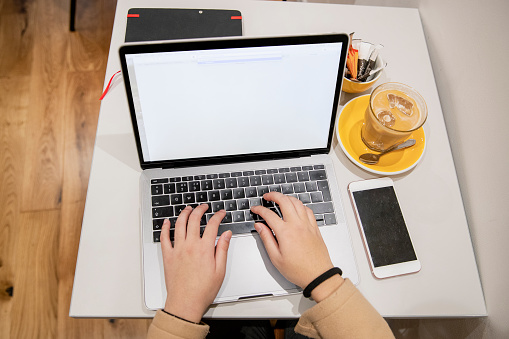 An aerial view of an unrecognisable people sat with a iced coffee and working on a laptop.