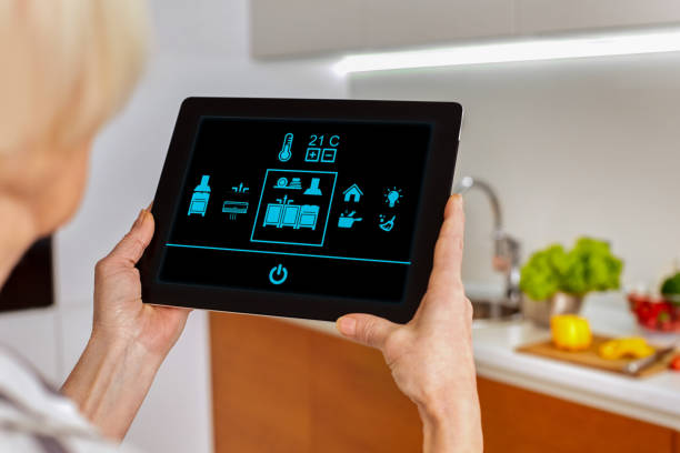 istock Smart home system kitchen control! Picture from back blurred background old woman hold tablet look on icons monitor device in fonteground. Touch fingers manage temperature room house interior. Mockup 1218961293
