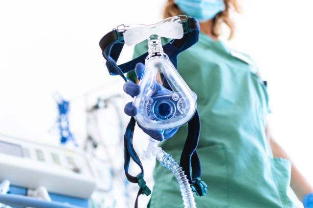 covid19 / 2019-ncov konzept: krankenschwester trägt eine maske der mechanischen lüftungsmaschine auf, die im vordergrund zu sehen ist. therapie zur lungenatmung auf der intensivstation. - oxygen stock-fotos und bilder
