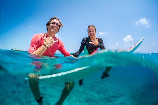 Young happy surfers man and woman sit on the surfboards in the water