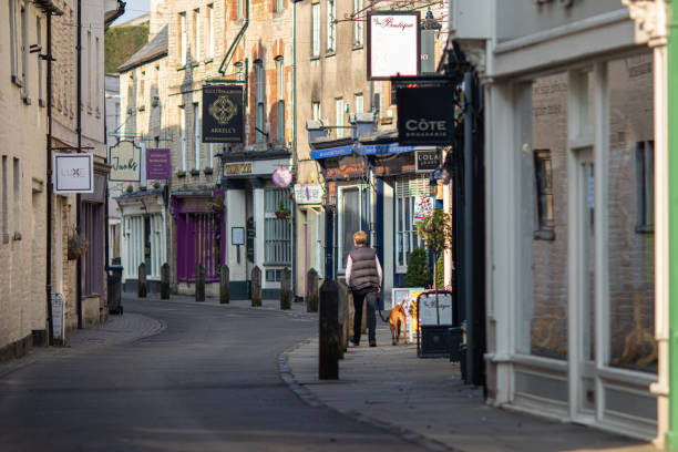 mujer solitaria paseando a su perro por la pintoresca calle black jack desierta en cirencester, gloucestershire durante el brote de coronavirus durante la primavera de 2020 - 2839 fotografías e imágenes de stock