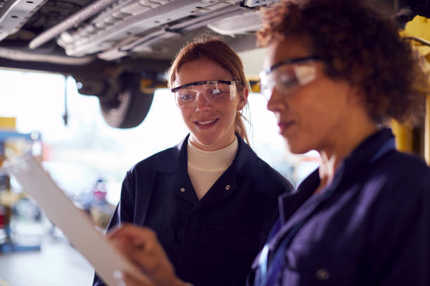 istock Female Tutor With Student Looking Underneath Car On Hydraulic Ramp On Auto Mechanic Course 1218969980