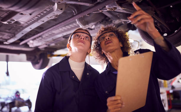 istock Female Tutor With Student Looking Underneath Car On Hydraulic Ramp On Auto Mechanic Course 1218970121