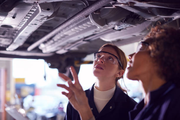 istock Female Tutor With Student Looking Underneath Car On Hydraulic Ramp On Auto Mechanic Course 1218970242