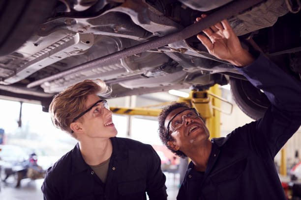 istock Male Tutor With Student Looking Underneath Car On Hydraulic Ramp On Auto Mechanic Course 1218970730
