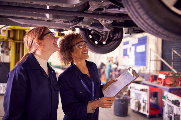 istock Female Tutor With Student Looking Underneath Car On Hydraulic Ramp On Auto Mechanic Course 1218971671
