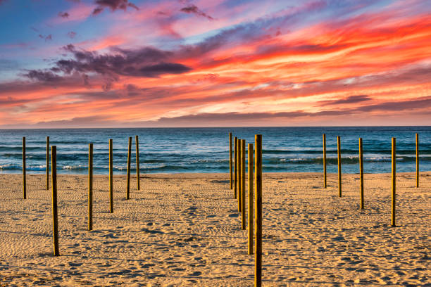 マヨルカ島の地中海の島のサコマのビーチでは、パラソルのための木製のポールは、背景に美しい夕日と砂の中に立ち往生しています ストックフォト