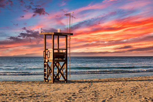 A lifeguard tower stands on the beach on the Mediterranean island of Mallorca with a beautiful colourful sunset