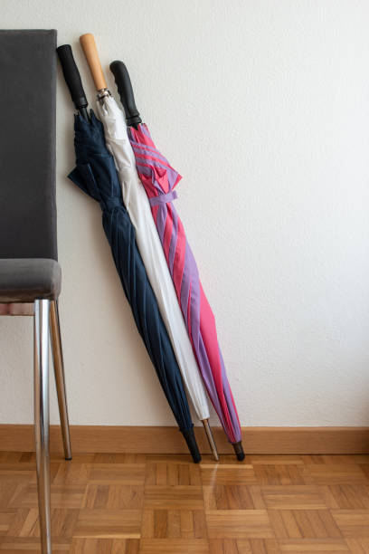 istock Tree folded large colorful umbrellas leaning on a chair set against white wall inside a room 1218973623