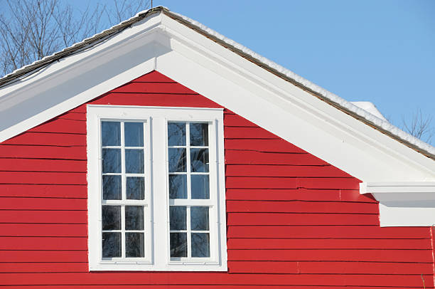 A close-up shot of a vibrant red textured wooden exterior wall of a Canadian cottage. A narrow white-framed window showcases a handcrafted hanging ornament made of natural driftwood and beads. This image evokes a sense of rustic charm, coastal living, and traditional craftsmanship common in lakeside retreats across Canada.