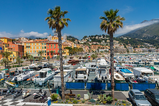 Menton, France - June 05, 2019: View of palm tree and harbor with boats in Menton on French Riviera. Provence-Alpes-Cote d'Azur, France.