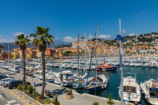 Menton, France - June 05, 2019: View of palm tree and harbor with boats in Menton on French Riviera. Provence-Alpes-Cote d'Azur, France.