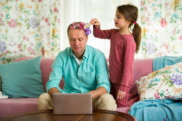 Child playing and disturbing father working remotely from home. Child playing and disturbing father working remotely from home. Little girl combing daddy's hair and making hairstyle. Man sitting on couch with laptop. Family spending time together indoors. combing photos stock pictures, royalty-free photos & images