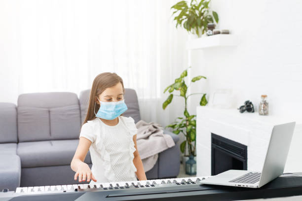 istock Little girl in protective mask learning the piano during quarantine. Coronavirus concept. 1218979372