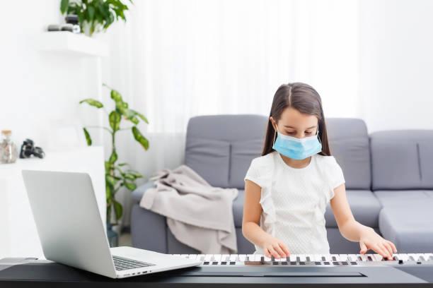 istock Little girl in protective mask learning the piano during quarantine. Coronavirus concept. 1218979416