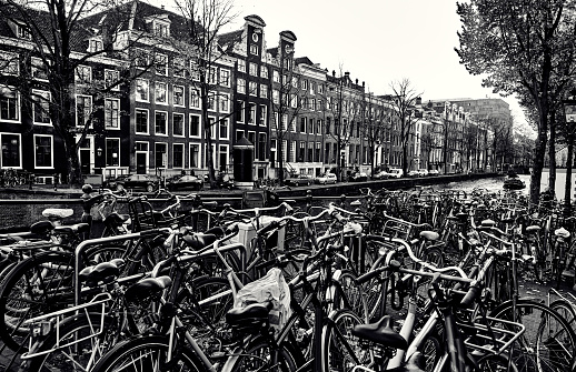 Many bicycles in the parking lot by the canal in Amsterdam. Black-white cityscape.