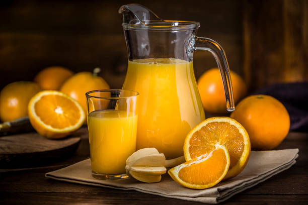 Orange juice Front view of a pitcher and a drinking glass full of orange juice surrounded by whole and sliced oranges. Low key DSLR photo taken with Canon EOS 6D Mark II and Canon EF 24-105 mm f/4L freshly squeezed stock pictures, royalty-free photos & images