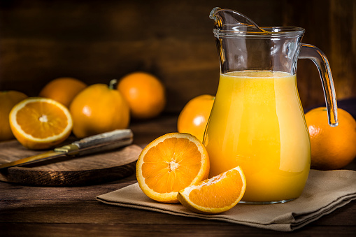 Front view of a pitcher full of orange juice surrounded by whole and sliced oranges. Low key DSLR photo taken with Canon EOS 6D Mark II and Canon EF 24-105 mm f/4L