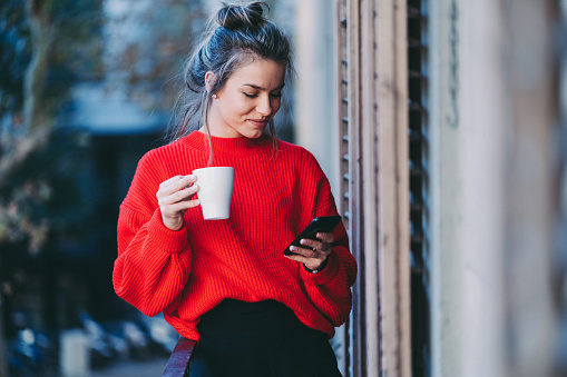 Female in Barcelona drinking coffee at the terrace and checking social media on phone