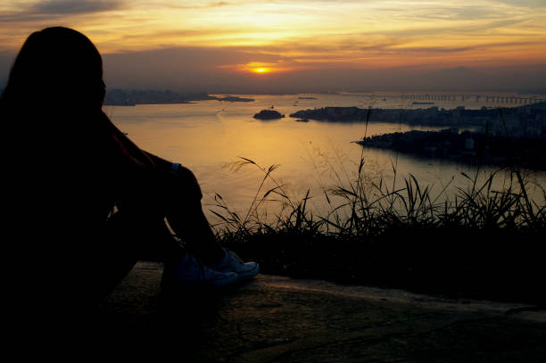 kobieta odpoczywająca na zachodzie słońca w miastach niteroi i rio de janeiro w brazylii. widok na miejsca turystyczne w miastach, takich jak zatoka guanabara - brazil silhouette sunset guanabara bay zdjęcia i obrazy z banku zdjęć