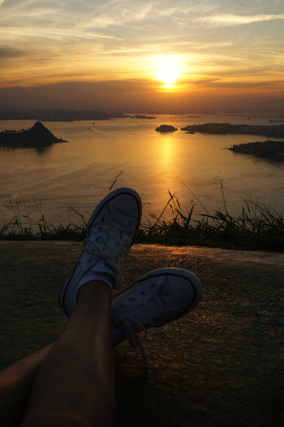 nogi kobiety odpoczywają o zachodzie słońca w miastach niteroi i rio de janeiro w brazylii. widok na miejsca turystyczne w miastach - brazil silhouette sunset guanabara bay zdjęcia i obrazy z banku zdjęć